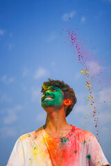 Close up of a young indian boy with his face covered in yellow and green holi colors.