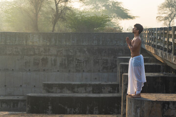 A young indian boy worshiping and praying early in morning wearing a white colored dhoti. God and religion concept.