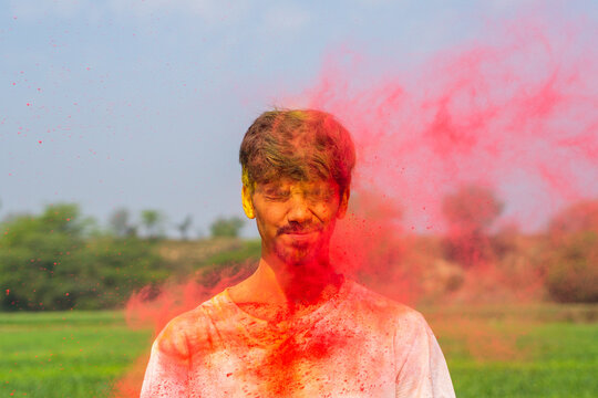 Young indian boy covered in holi colors, boy playing holi with a colored smoke bomb.
