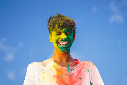 Portrait of a young indian boy playing holi. Face covered in Holi colors with a beautiful blue sky in background. Copy space for graphics and text.