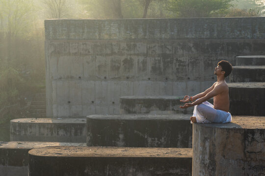 Young indian boy praying to god early in the morning. Young boy doing yoga during sunrise wearing a white dhoti. Religion and health concept.