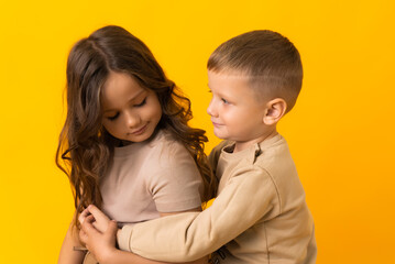 A little brother is hugging his older sister in the studio on a yellow background