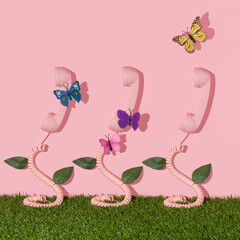 Spring creative layout with pink retro phone handset with colorful butterflies, leaves on pastel pink background with green grass. 80s or 90s retro fashion aesthetic telephone and flowers concept. 
