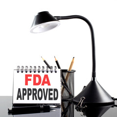 FDA Approved text on notebook with pen and table lamp on the black background
