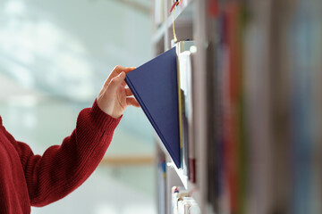 Female hand pulling book from bookshelf in public library in university, college or high school....