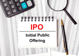 On the table are reports and a white notebook with the text IPO Initial Public Offering.