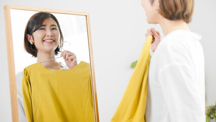 鏡の前で服選びをしている若い女性　ファッションイメージ