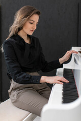 Portrait of a young beautiful female musician in a casual shirt playing the white grand piano on black background