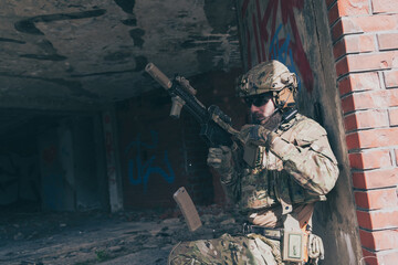 A bearded soldier in special forces uniform in dangerous military mission, refile his weapon while hiding from the wall. Selective focus 