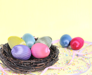 Easter homemade eggs from satin ribbons in a nest on a yellow background