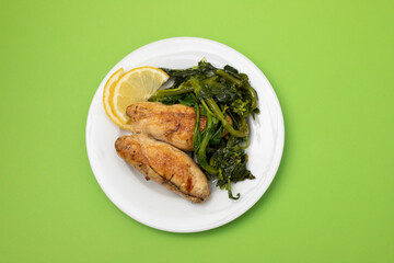 Grilled caviar cod fish with greens and fresh lemon on white small plate.