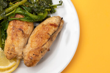 Grilled caviar cod fish with greens and fresh lemon on white small plate.