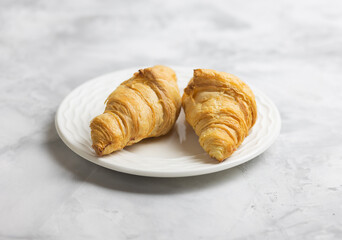 Two delicious croissants on a plate . Morning French breakfast with fresh pastries. Light gray background.