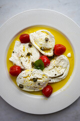 Horizontal flat lay of classic italian caprese salad with sliced tomatoes, mozzarella, basil, olive oil, pepper, salt and toast. Rustic mediterranean meal on light background