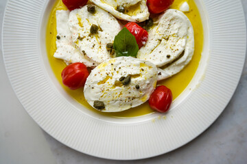 Horizontal flat lay of classic italian caprese salad with sliced tomatoes, mozzarella, basil, olive oil, pepper, salt and toast. Rustic mediterranean meal on light background