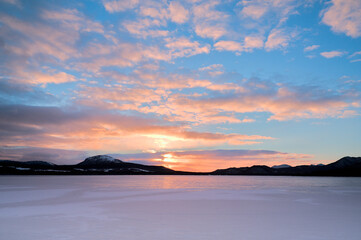 夜明けの雪原の上に広がるカラフルな空。冬の北海道の雪に覆われた屈斜路湖。