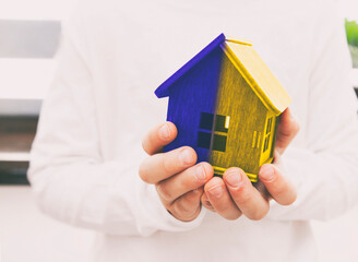 Kid holding wooden toy house in Ukrainian flag colors