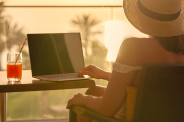 Silhouette of woman freelancer in straw hat drinking juice during working on laptop sitting on the...