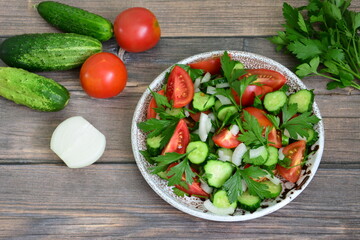 vegetable salad with tomatoes, cucumber, onion and parsley in bowl on wooden background