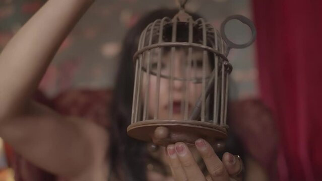 Close up video of a woman with the dark red lipstick spinning a small metal cage with a large key inside