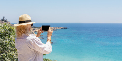 A tourist woman in a white dress and with hat enjoys the beautiful, turquoise Sea of Greece during her summer holiday. Banner with copy space.