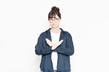 白い背景の前に立ってNGのジェスチャーをする眼鏡をかけている女性