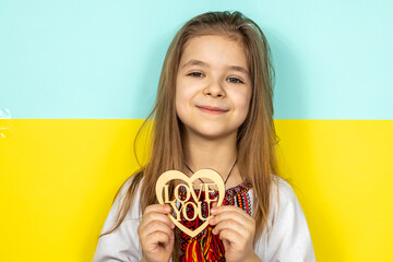 A girl in national Ukrainian clothes, vyshyvanka, holds a wooden heart as a sign of love for...