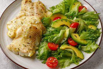 Healthy vegetarian food. Dinner with halibut fish and green salad with frillis leaves, tomatoes, avocado.