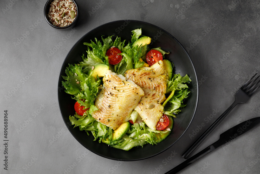 Wall mural dish with gourmet fried halibut fish on vegetable, fresh green salad. top view. black plate.