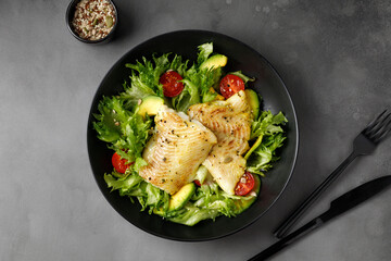 Dish with Gourmet fried halibut fish on Vegetable, fresh green salad. Top view. Black plate. - obrazy, fototapety, plakaty