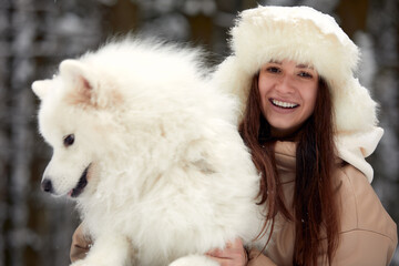 Happy young woman in winter, holds in her arms and plays in the snow with her pet dog