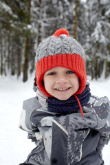 Fototapeta na wymiar Child playing with snow in winter. Little boy in colorful jacket and knitted hat catching snowflakes in winter park on Christmas. Kids play and jump in snowy forest. Children catch snow flakes