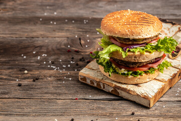 homemade burger with grilled meat, vegetables, sauce on rustic wooden background. fast food and junk food concept