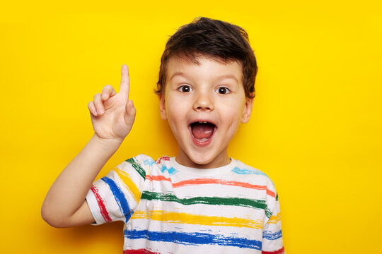 idea. child, boy emotionally points up. A gesture of an idea. Portrait of a child in a bright striped T-shirt on a yellow background