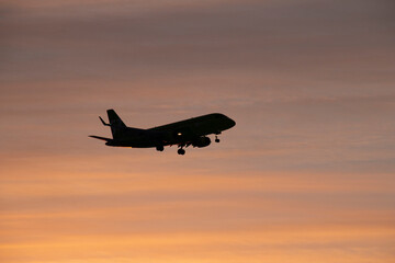 The plane comes in to land at the airport against the background of dawn. Passenger airliner flying at low altitude with landing gear released against the background of dawn