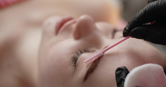 The beautician brushes the woman's brows by eyebrow brush, henna colorising, brows spa, 4k 60p