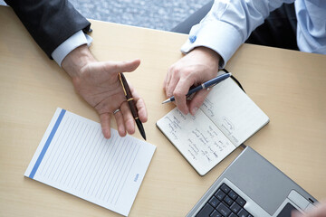 Two business men hold pens in their hands make notes in a notebook and in a laptop during negotiations