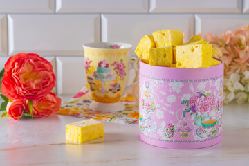yellow marshmallows in a beautiful pink box, spring pink flowers in the background, elegant cup