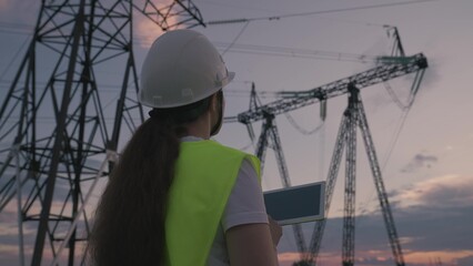 young specialist woman in hardhat. electrical engineer controls work by tablet at sunset. concept...