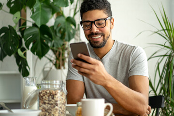 Happy black man using mobile phone while eating breakfast. People technology gadget concept