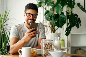 Young black man eating breakfast and reading the news online. Handsome man using mobile phone