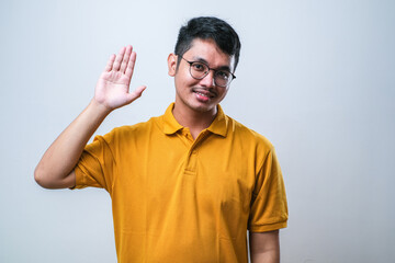 Young handsome asian boy waiving saying hello happy and smiling, friendly welcome gesture