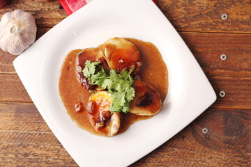 Egg with Tamarind Sauce in a white plate served on a wooden table with coriander sprinkles, is a popular local dish that Thai people eat.