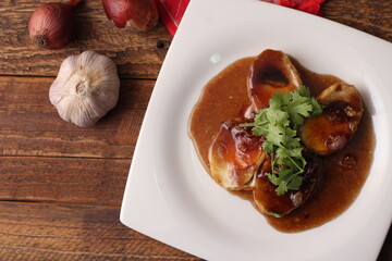 Egg with Tamarind Sauce in a white plate served on a wooden table with coriander sprinkles, is a popular local dish that Thai people eat.
