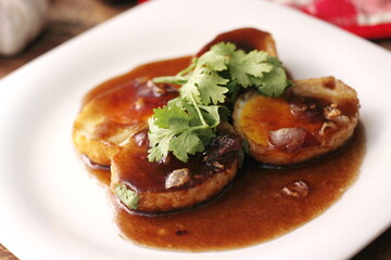 Egg with Tamarind Sauce in a white plate served on a wooden table with coriander sprinkles, is a popular local dish that Thai people eat.