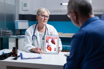 Obraz premium Physician explaining cardiology diagnosis with image of heart organ on tablet to patient. General practitioner showing illustration on cardiovascular system and anatomical structure to man.