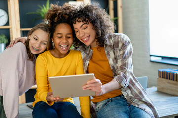 Group of multiethnic teenage friend girls are using gadgets, talking and smiling together.