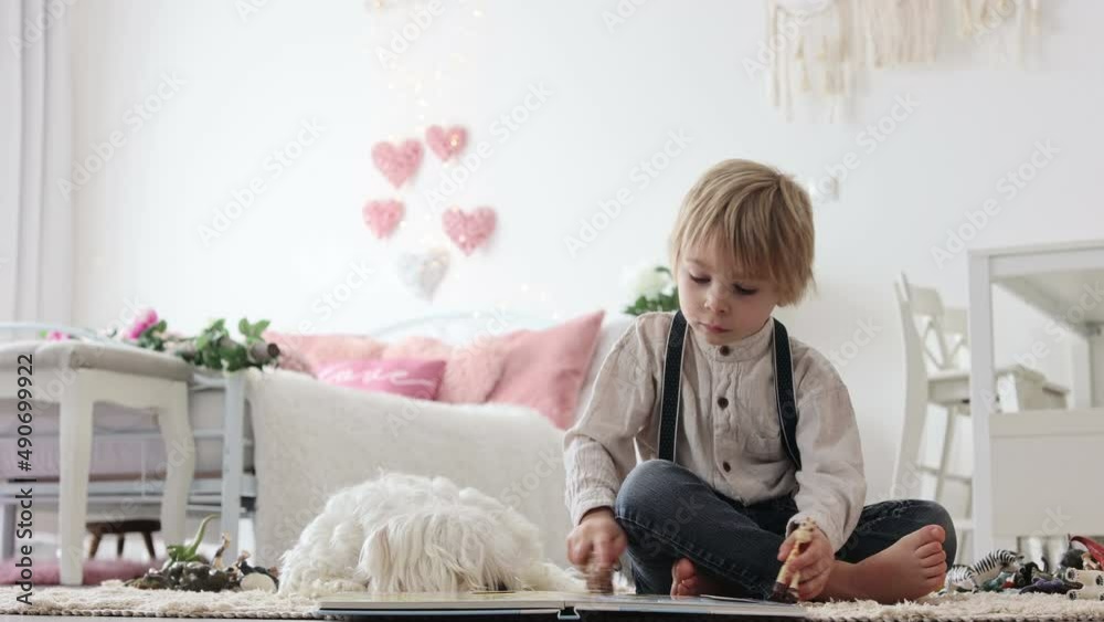 Wall mural Cute blond preschool child, blond boy with pet maltese dog, reading book at home on the floor with mother