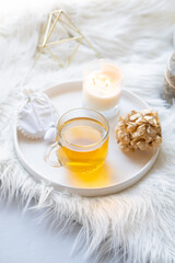 Cup of herbal tea and burning candle on round white decorative tray