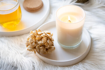Cup of herbal tea and burning candle on round white decorative tray